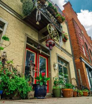 A charming storefront with red doors, vibrant potted plants, and decorative accents like a wagon wheel and hanging lanterns.